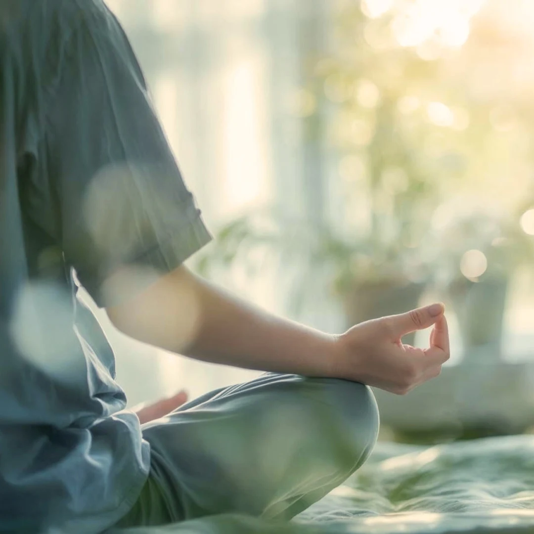 Untitled design (8) Person seated cross-legged in meditation posture outdoors against nature backdrop